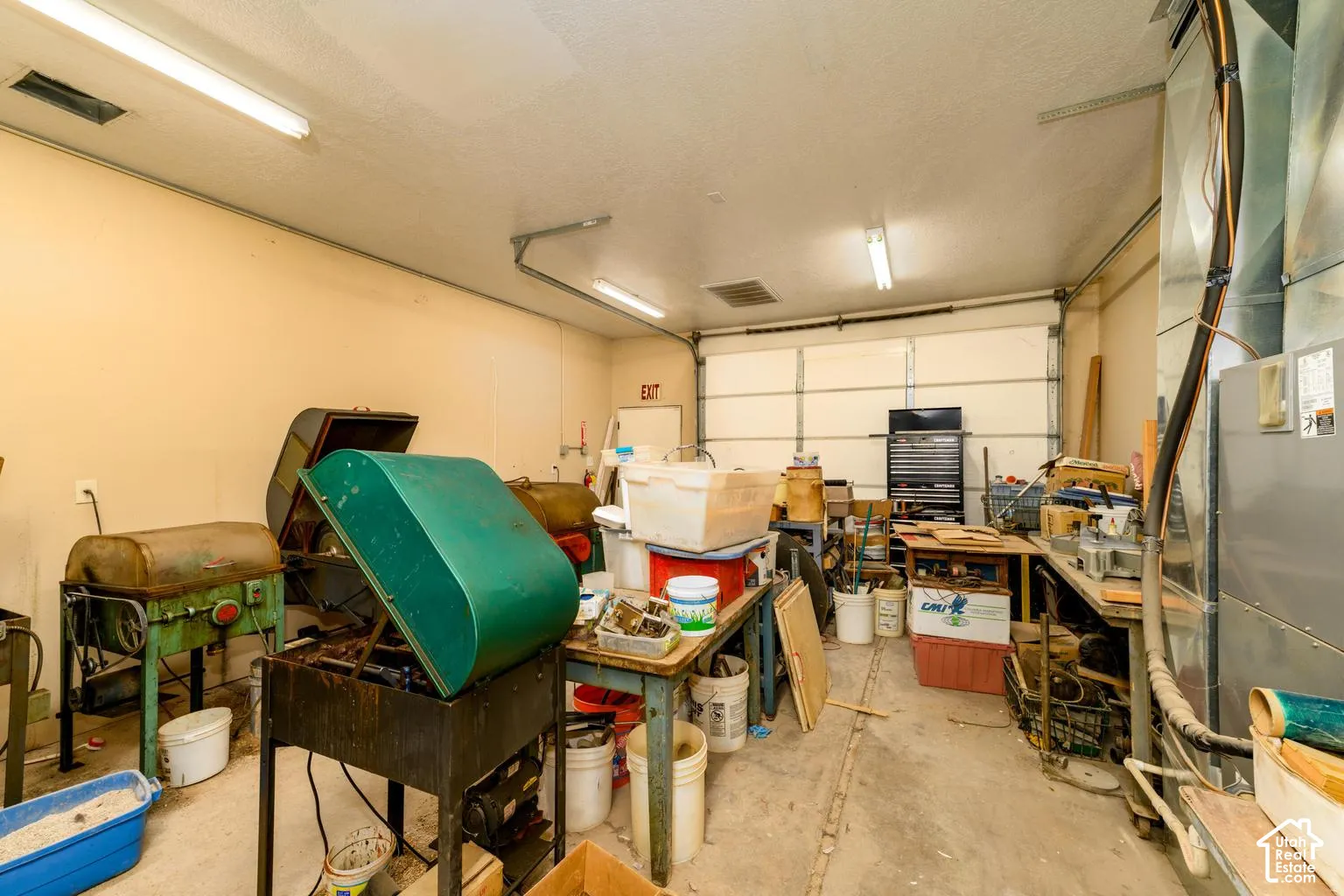 Garage space with a roll-up door, exposed ductwork, and fluorescent lighting