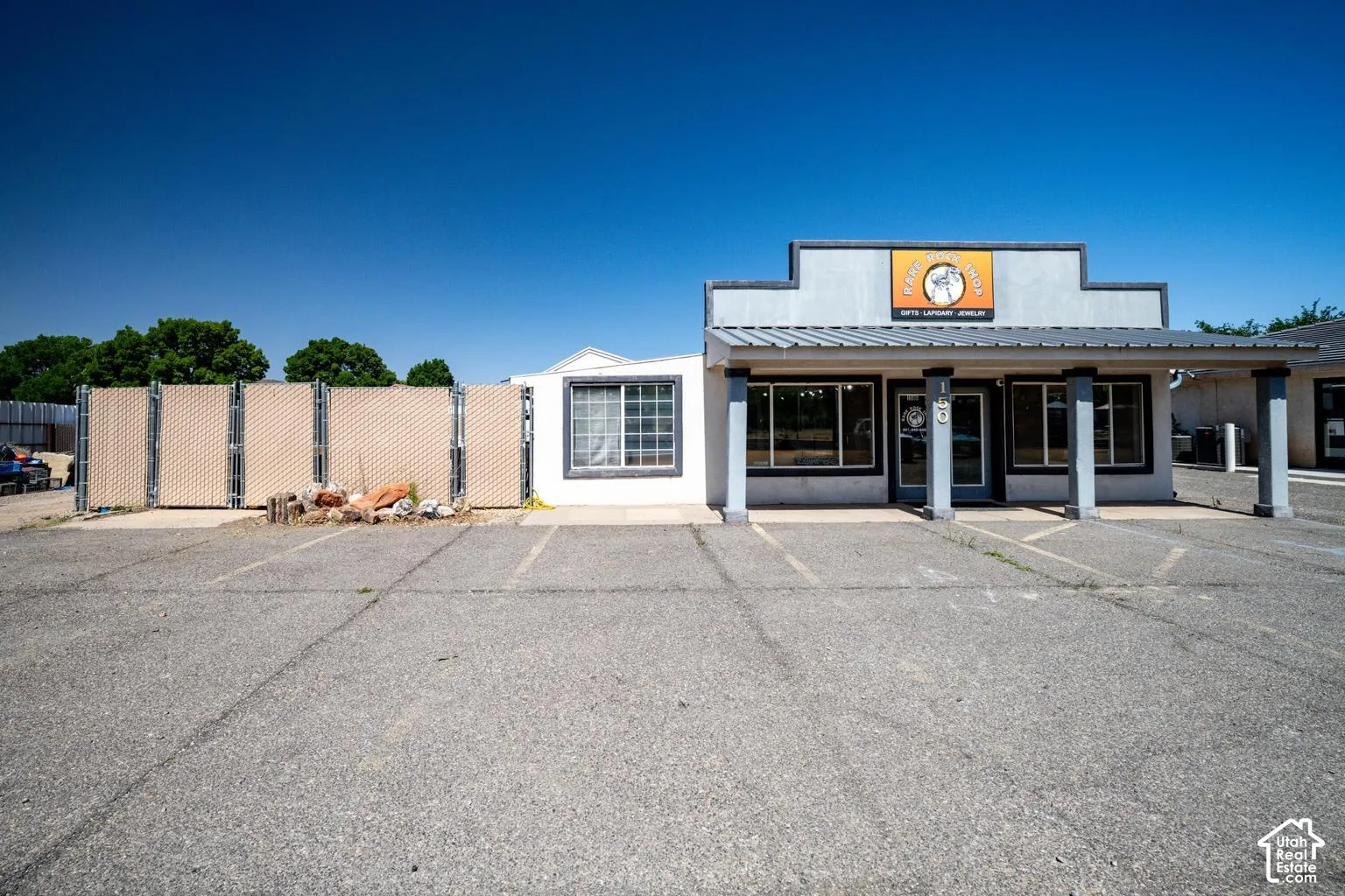 Asphalt parking area with painted space lines, a white stucco building with multiple windows, and an awning supported by columns