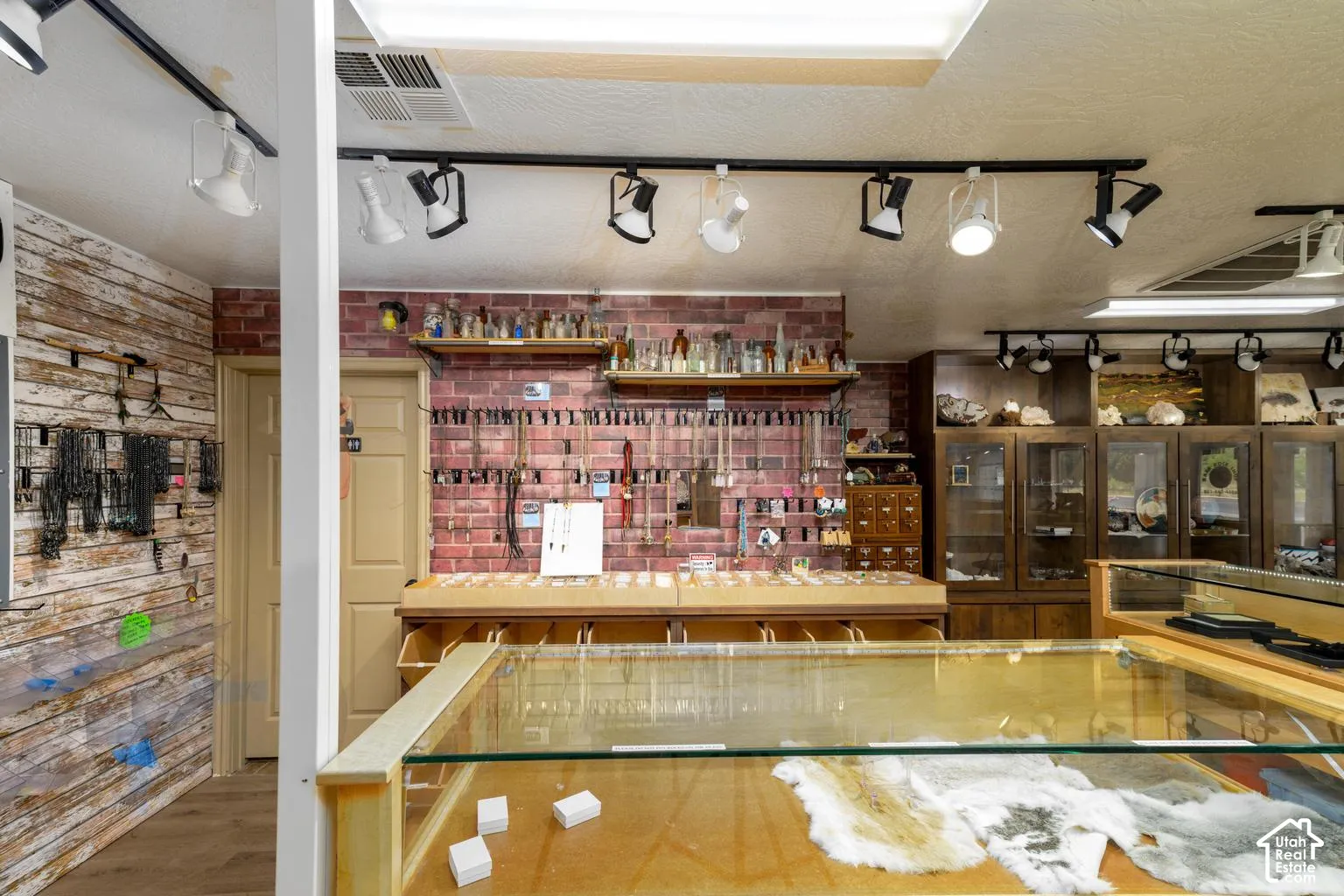 Track lighting fixtures, wood-finish flooring, exposed brick wall, built-in wooden display cabinets, and glass display cases