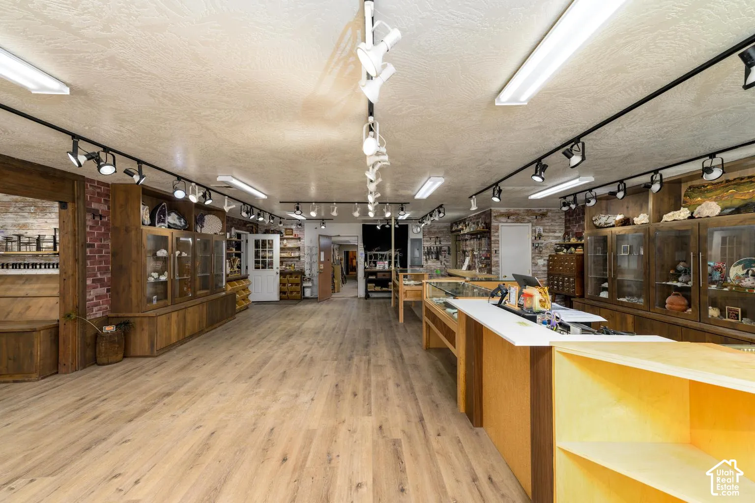 Expansive interior space featuring wood-finish flooring, track lighting, built-in wooden display cases, and a service counter