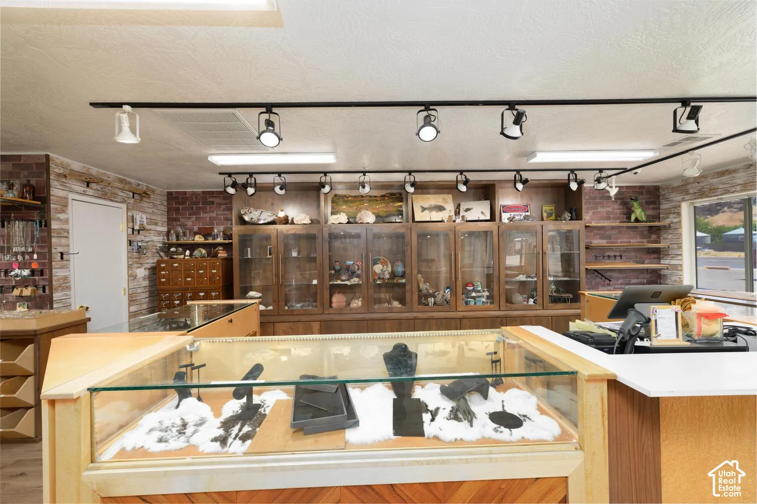 Track lighting system, wood-finish flooring, brick accent wall, wood-finish display cases, and a white countertop
