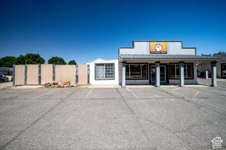 Asphalt parking area with painted space lines, a white stucco building with multiple windows, and an awning supported by columns