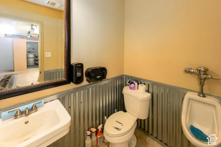 Bathroom featuring a white toilet, white wall-mounted urinal, and a white sink with a brushed nickel faucet