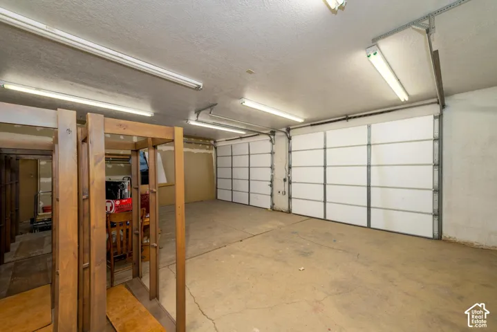 Concrete floor garage featuring two white paneled overhead doors and fluorescent ceiling lighting
