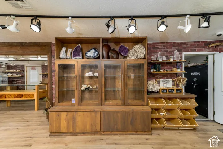 Wood-finish flooring, exposed brick accent wall, track lighting, built-in wooden cabinetry with glass-front uppers, and open shelving