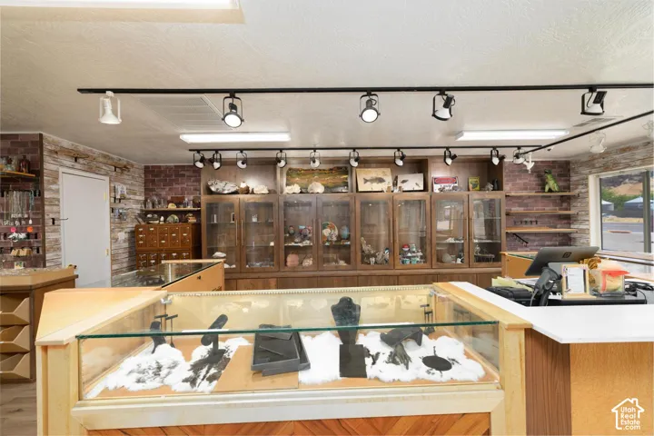 Track lighting system, wood-finish flooring, brick accent wall, wood-finish display cases, and a white countertop