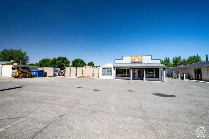 Commercial building with a metal roof and storefront windows, accompanied by a large paved parking area