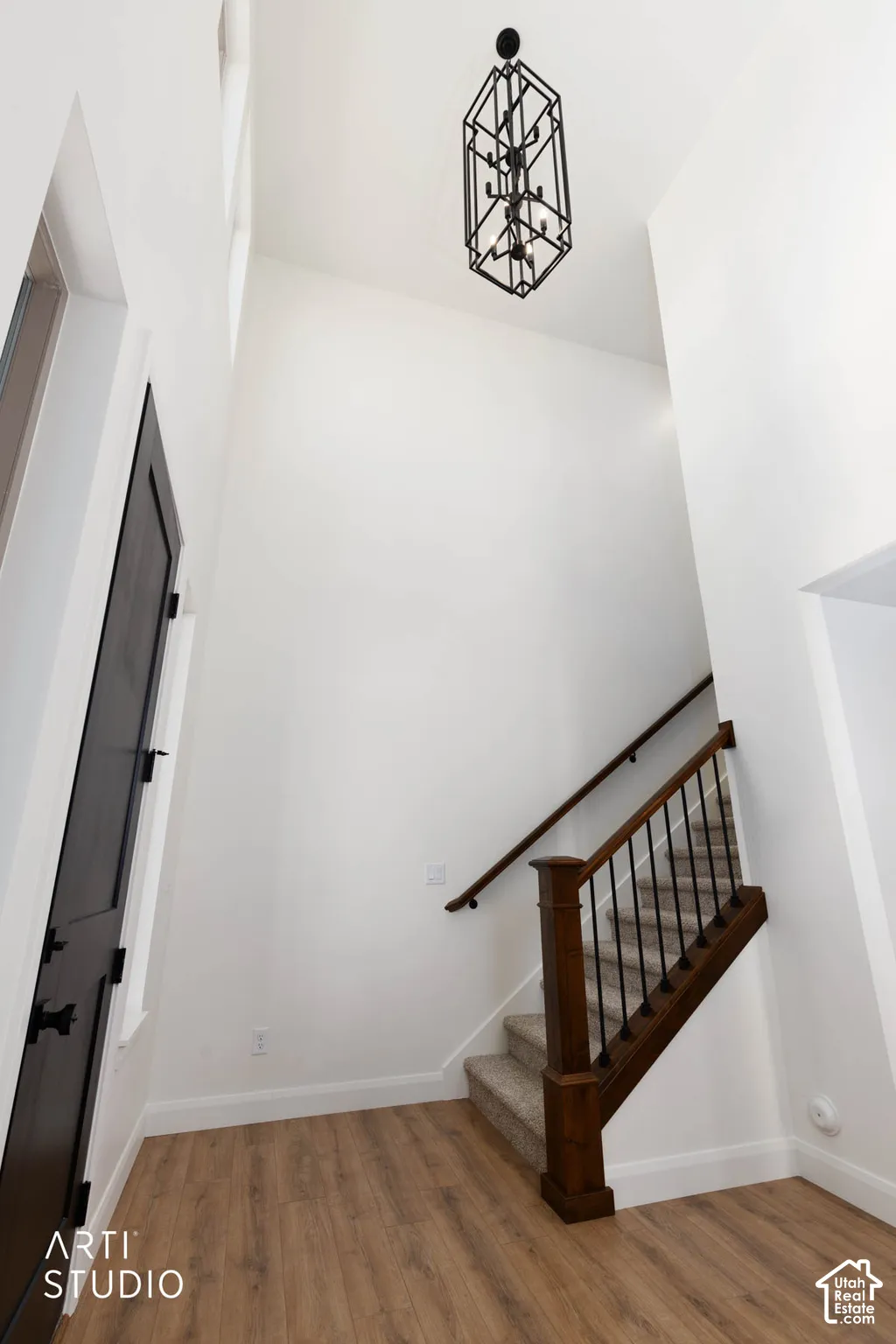 Wood-finish flooring, staircase with dark wood newel post and balusters, dark handrail, and elegant black geometric chandelier