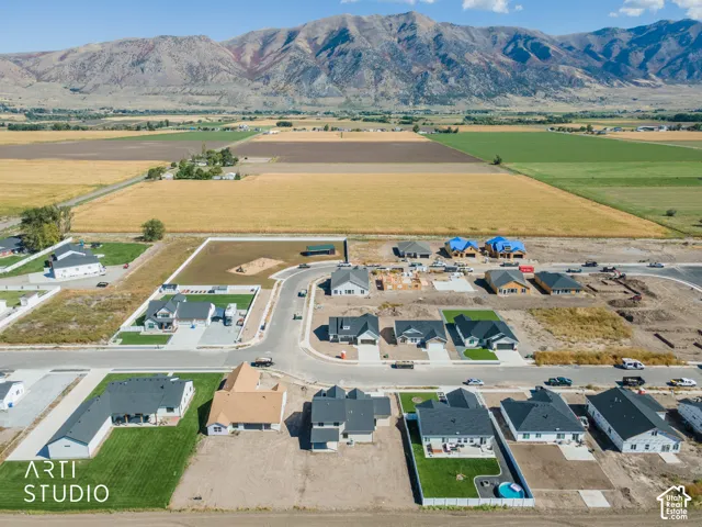 Expansive mountain backdrop, agricultural fields, developed residential street, and new construction homes