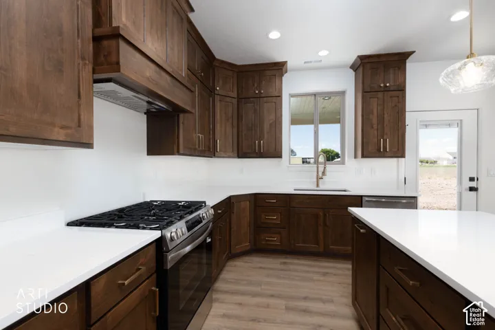 Custom cabinetry with brushed gold hardware, stainless steel range and hood, white countertops, wood-finish flooring, and recessed lighting