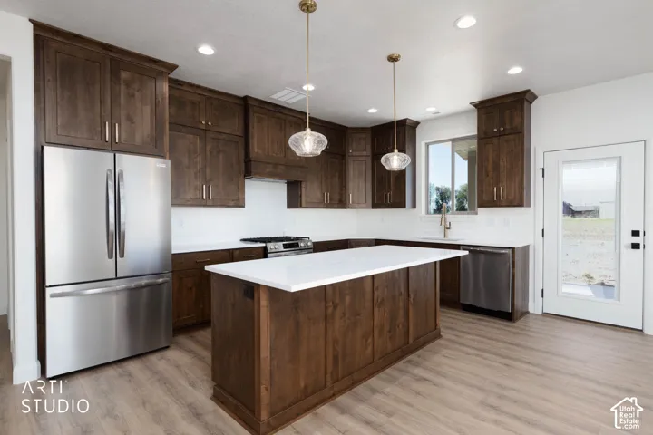 Expansive kitchen featuring wood-finish flooring, dark wood cabinetry, stainless steel appliances, a center island with a white countertop, and recessed lighting