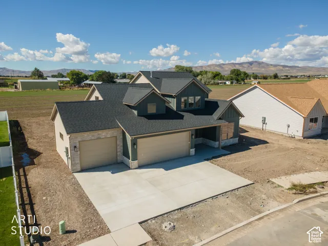 Multi-pitch dark shingle roof, two-car garage with light tan doors, stone facade accents, dark vertical siding, and a concrete driveway