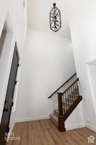 Wood-finish flooring, staircase with dark wood newel post and balusters, dark handrail, and elegant black geometric chandelier