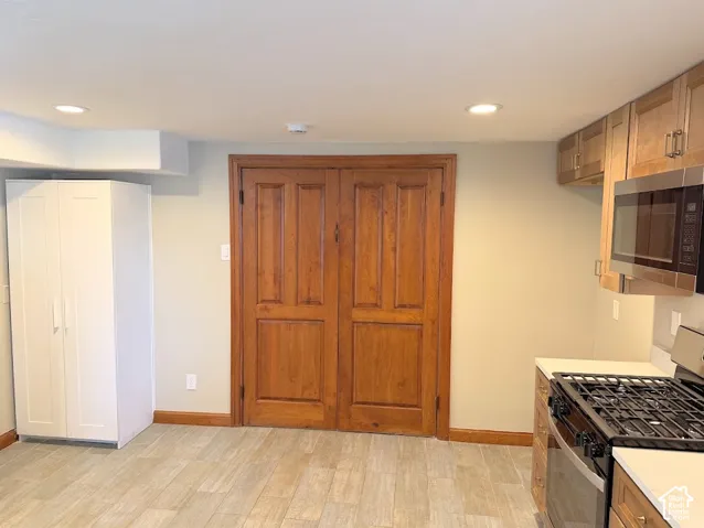 Recessed lighting, wood-finish flooring, wood cabinetry, stainless steel microwave, and stainless steel range