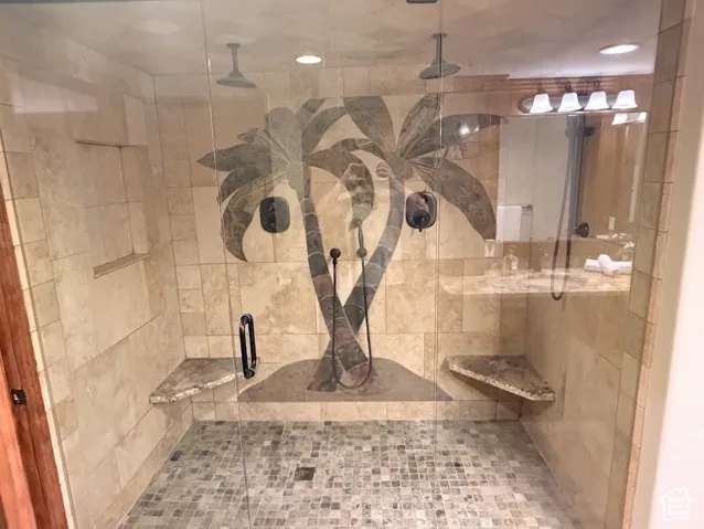 Spacious shower with glass enclosure, dual rain shower heads, mosaic tile floor, and built-in corner benches
