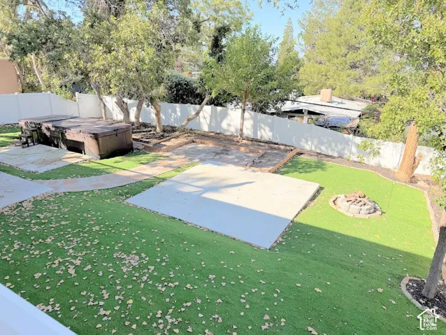 Expansive backyard featuring artificial turf, concrete patio pads, a built-in fire pit, and a privacy fence