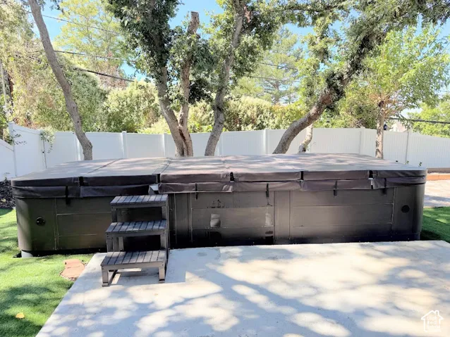 Outdoor spa with a protective cover, integrated steps, and a surrounding concrete patio