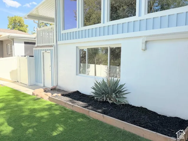Exterior featuring white stucco and vertical siding, turf lawn, and a raised planter with dark mulch
