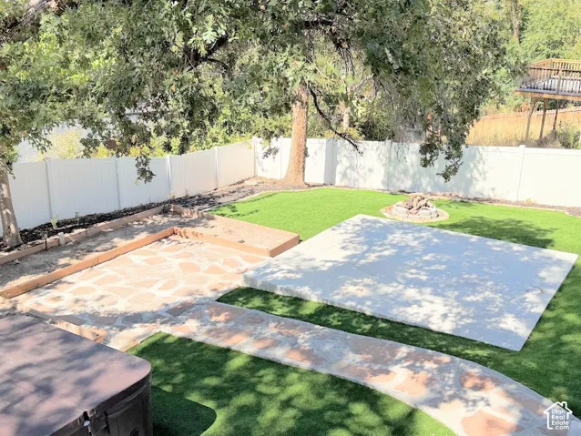 Expansive backyard featuring artificial turf, a white privacy fence, a concrete patio, a flagstone patio, and a built-in fire pit