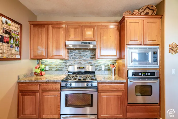 Stainless steel appliance suite, mosaic tile backsplash, granite countertops, and wood cabinetry