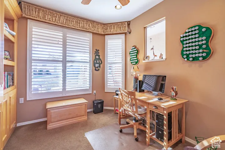 Built-in cabinetry, plantation shutters, natural wood-finish desk, and ceiling fan
