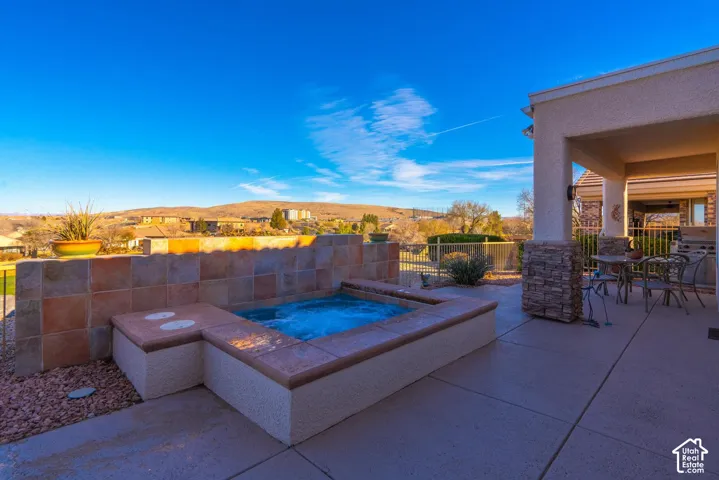 Outdoor patio with a built-in spa, tiled privacy wall, and covered dining area featuring a stone-clad column