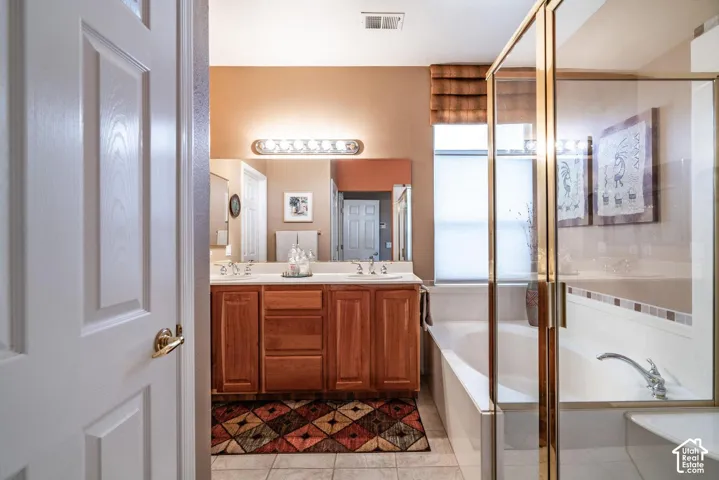 Bathroom with dual wood-finish vanity, integrated sinks, vanity lighting, and a built-in tub with a glass enclosure