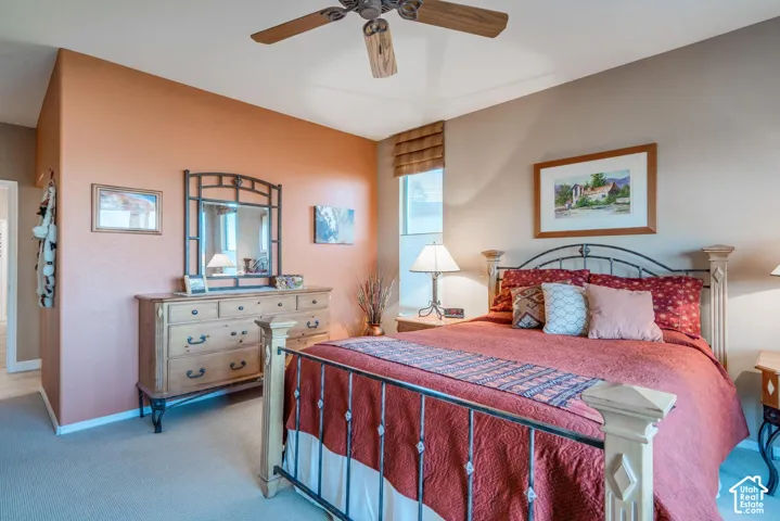 Carpeted flooring with a ceiling fan, window with shade, and a light-toned wood dresser featuring a mirror