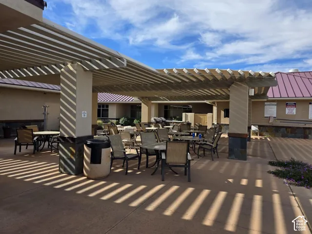 Expansive outdoor patio featuring a slatted pergola, stone veneer accents, and concrete paving