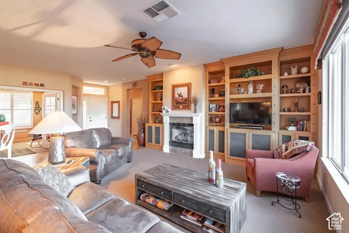 Living area with a ceiling fan, fireplace with a mantle, built-in shelving, and a large window