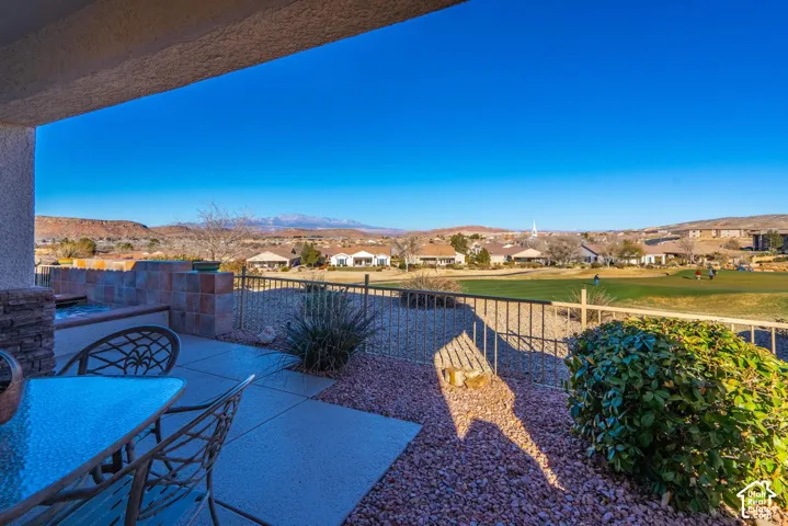 Covered outdoor patio with a built-in spa, concrete and gravel hardscaping, and a wrought iron fence overlooking a golf course