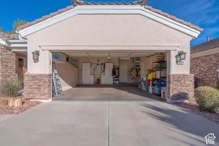Stucco exterior featuring stacked stone accents, a tile roof, and an attached garage with overhead lighting
