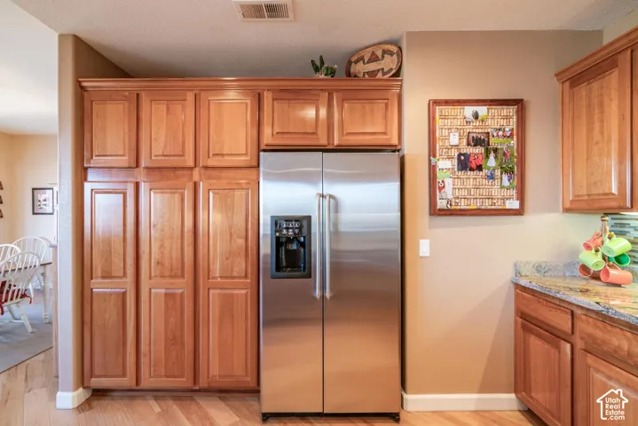 Stainless steel side-by-side refrigerator, extensive wood cabinetry, wood-finish flooring, and natural stone countertop