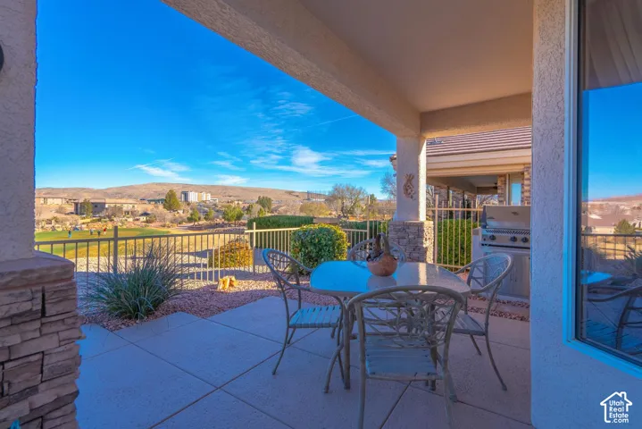 Covered patio with stone-accented columns, a built-in outdoor grill, and a tile floor, featuring a metal railing