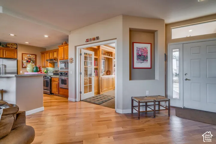 Wood-finish flooring throughout, kitchen with stainless steel appliances, recessed lighting, double French doors, and built-in shelving