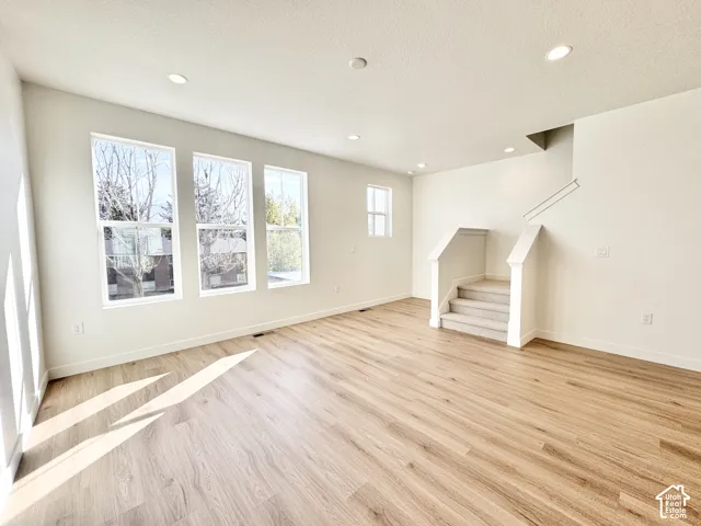 Spacious interior featuring wood-finish flooring, recessed lighting, and a staircase with carpeted treads