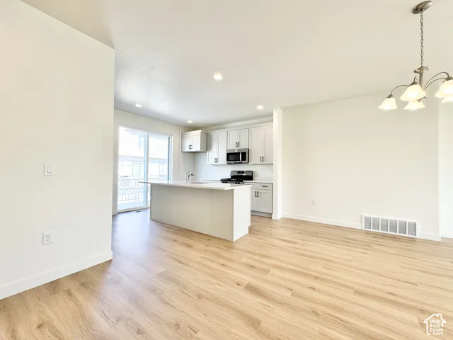 Light wood-finish flooring throughout, recessed lighting, white walls, kitchen island with solid surface countertop, and stainless steel appliances