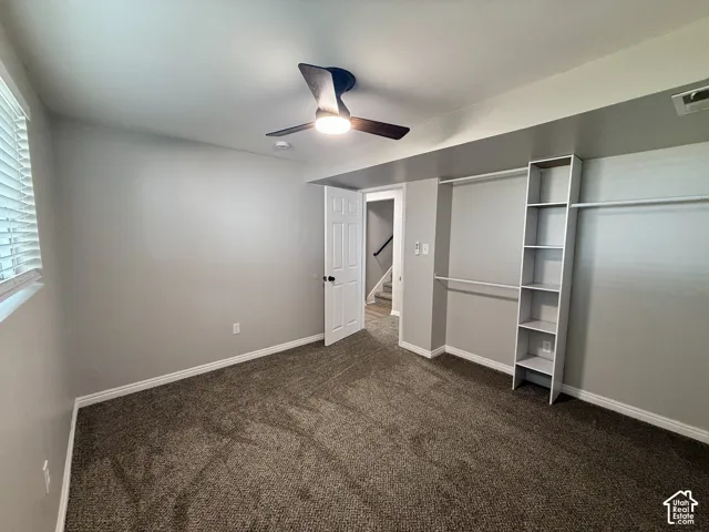Plush brown carpet, neutral painted walls, built-in closet shelving, and a ceiling fan with integrated lighting