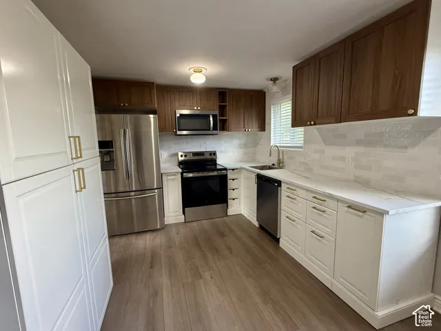 Kitchen featuring wood-finish flooring, two-tone cabinetry with gold-tone hardware, stainless steel appliances, and a tile backsplash