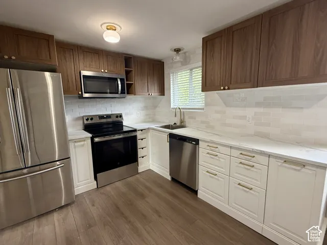 Kitchen featuring wood-finish upper cabinetry, white lower cabinetry, stainless steel appliances, a subway tile backsplash, and wood-finish flooring