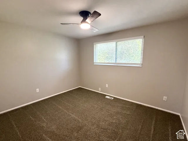 Carpeted flooring, neutral wall tones, ceiling fan with integrated lighting, and a large window with blinds