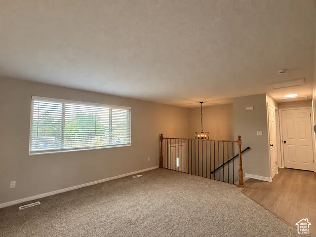 Carpeted living area with a large window, spindle railing, and a contemporary chandelier