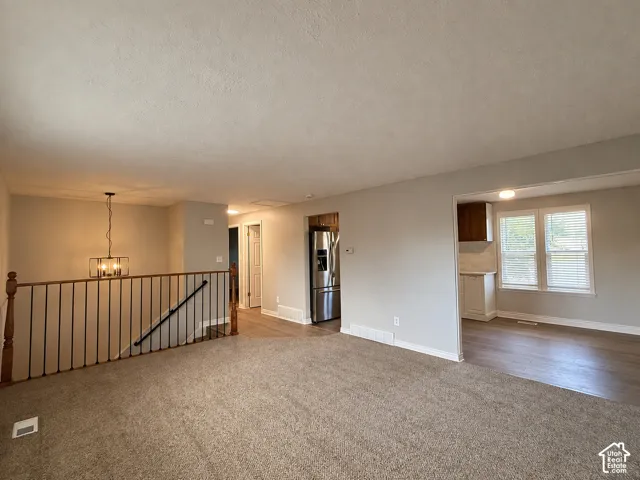 Open-concept living area with carpet flooring and a stairwell featuring a wood newel post and metal balusters