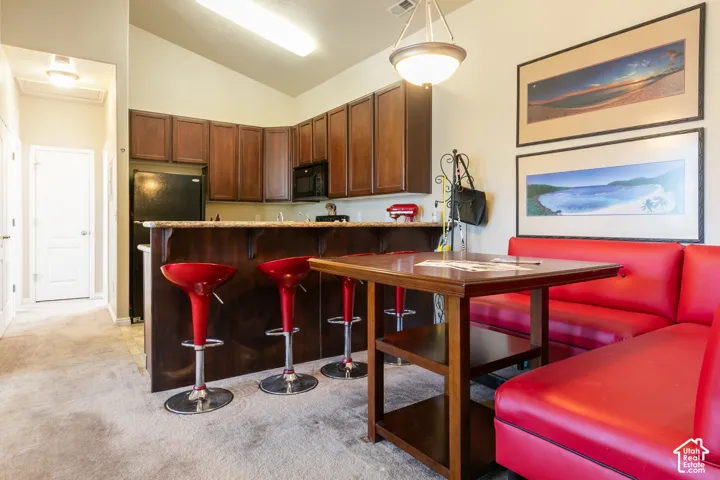 Kitchen featuring rich wood-finish cabinetry, black appliances, a counter-height breakfast bar with a stone-finish countertop, and a vaulted ceiling