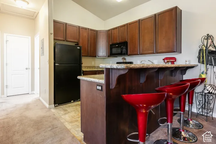 Kitchenette with wood-finish cabinetry, black appliances, and a breakfast bar with stone-finish countertops
