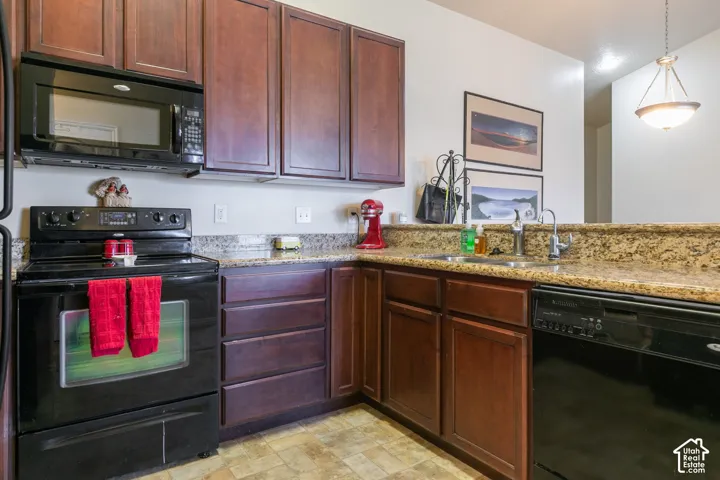 Kitchen featuring wood cabinetry, an undermount double-basin sink, granite-style countertops, and a full suite of black appliances, including a built-in microwave, range, and dishwasher