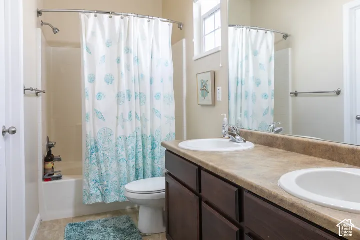 Bathroom featuring a dual-sink vanity with dark wood-finish cabinetry, a large mirror, and a shower-over-tub combination