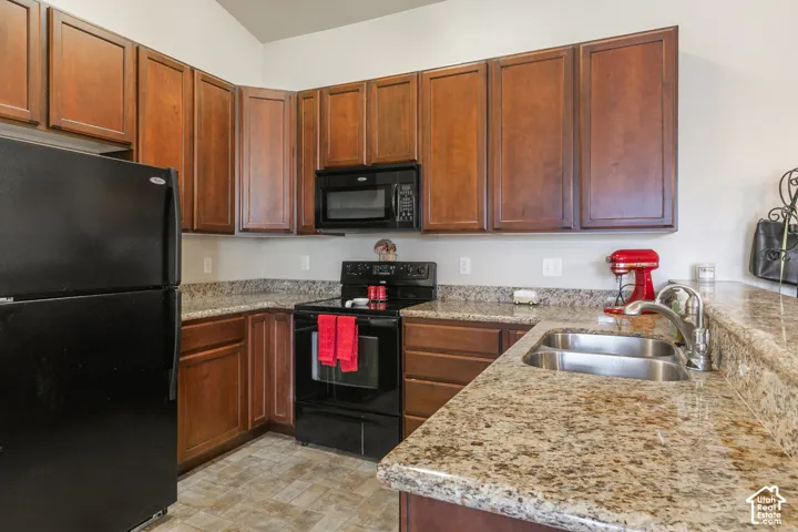 Kitchen featuring wood cabinetry, black appliances, granite-style countertops, a double basin stainless steel sink, and vinyl flooring