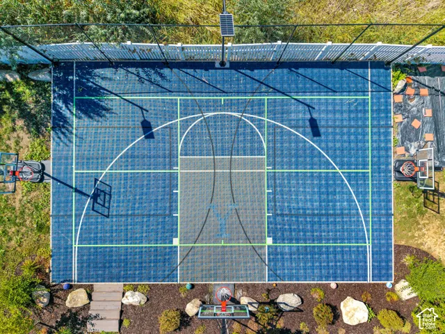Outdoor sports court with blue and gray surfacing, two basketball hoops, perimeter fencing, and a solar-powered light fixture