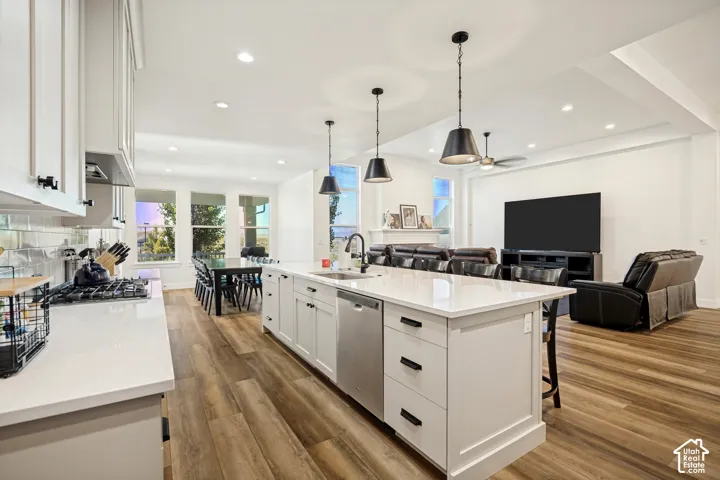 Spacious kitchen featuring an extended island with a built-in sink and dishwasher, white shaker cabinetry, white countertops, and wood-finish flooring